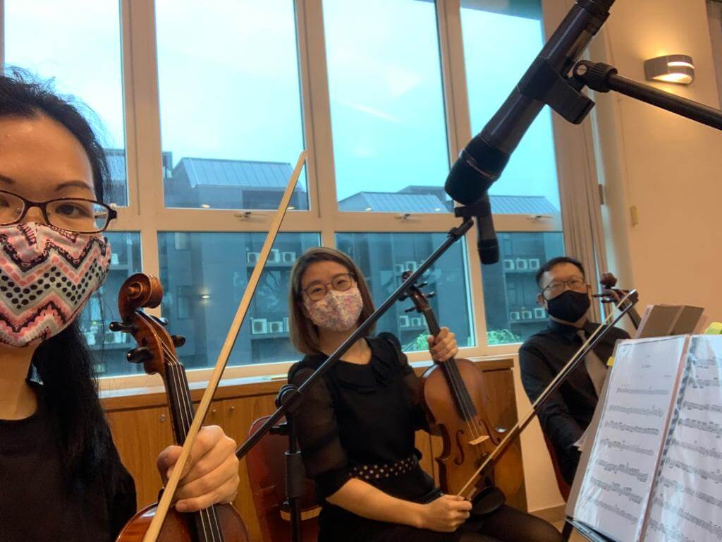 String players rehearsing beside a window, wearing masks