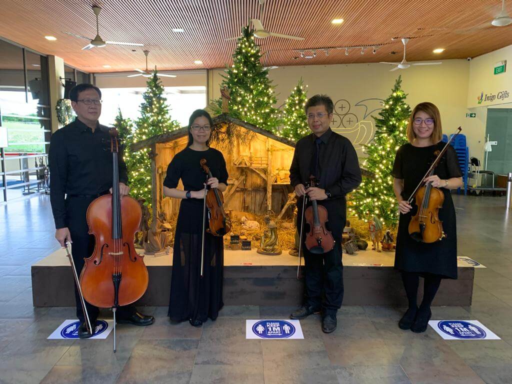 A string quartet performing on stage beside decorated Christmas trees