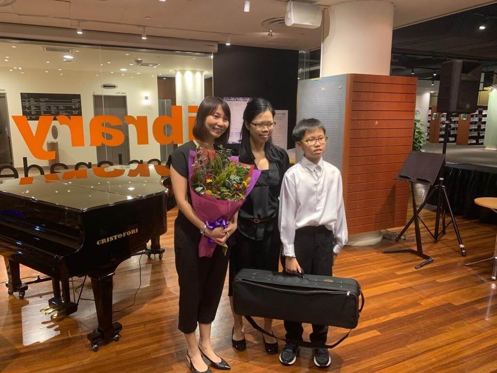 Violin students with flowers beside a grand piano after a recital